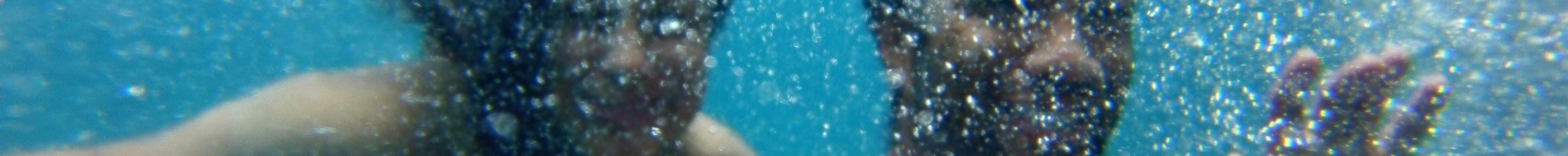 An underwater photo of two people smiling and waving happily with bubbles everywhere